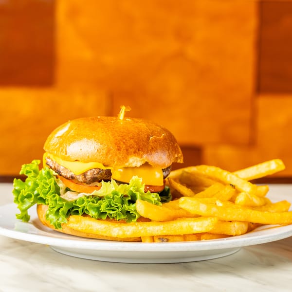 Cheeseburger with lettuce, tomato, and fries on a white plate against an orange background.