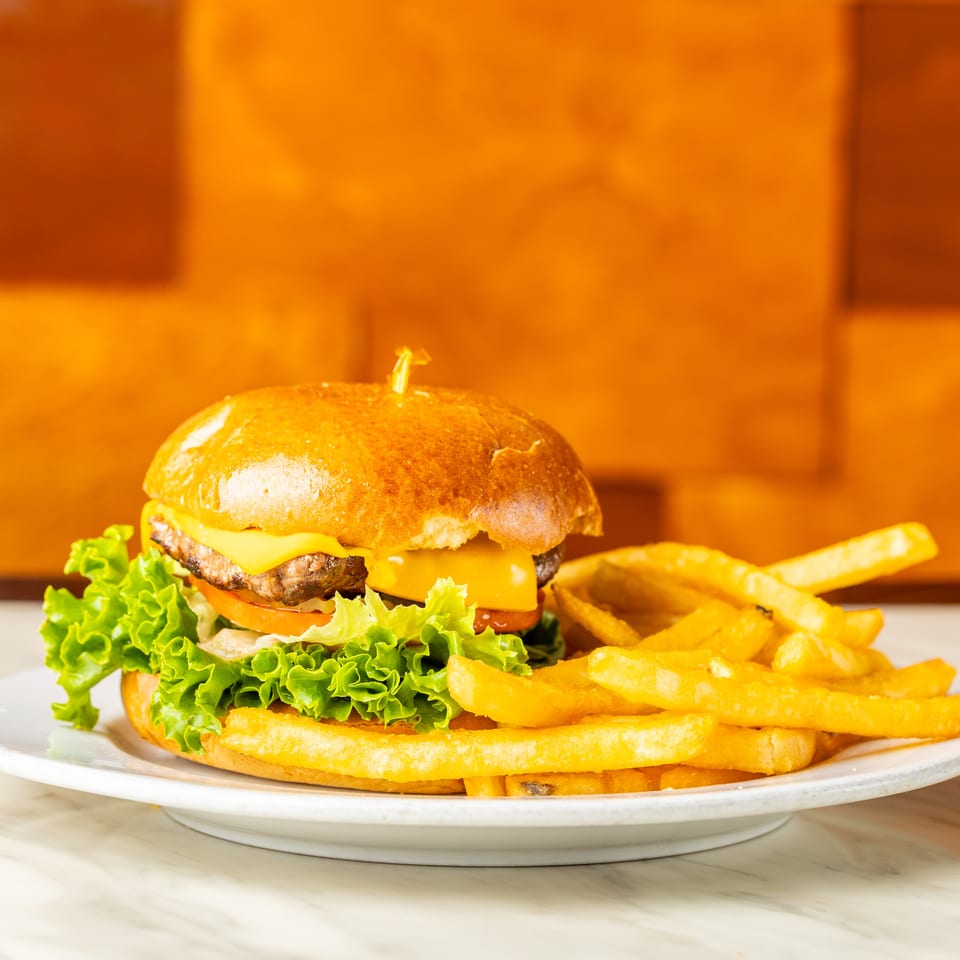 Cheeseburger with lettuce, tomato, and fries on a white plate against an orange background.