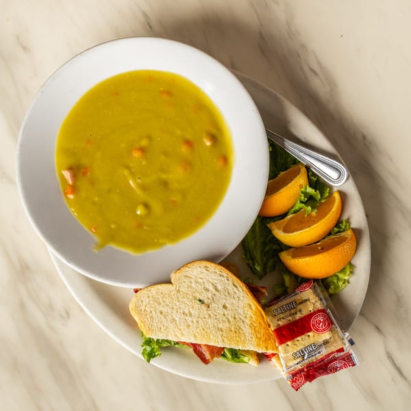 Split pea soup with a bacon sandwich, orange slices, and saltine crackers on a white plate.