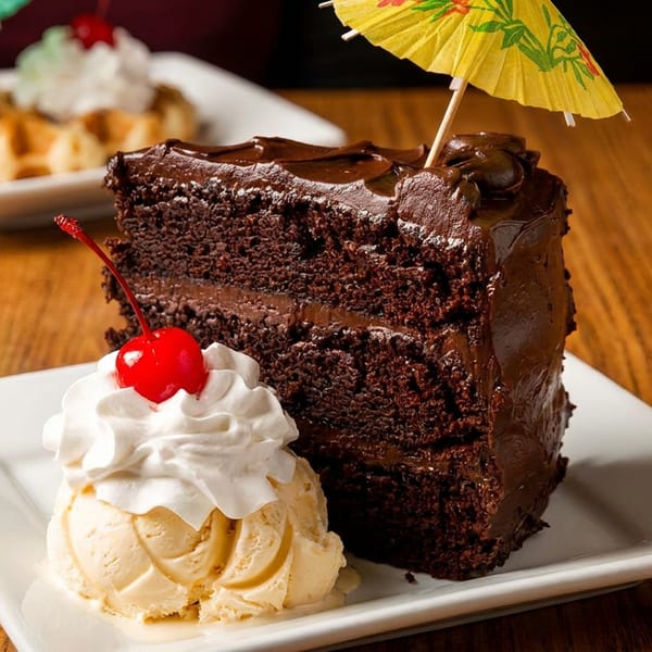 Decadent chocolate cake slice with vanilla ice cream, whipped cream, cherry, and a yellow umbrella.