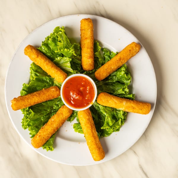 Golden-brown mozzarella sticks arranged in a circle on lettuce with a side of marinara sauce.