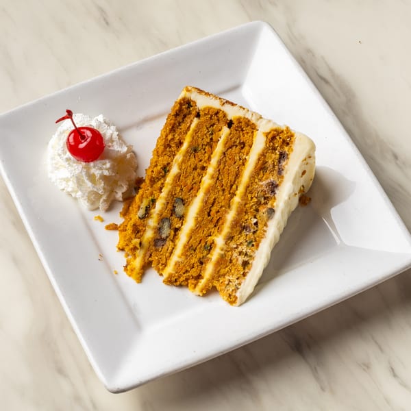 A slice of carrot cake with cream cheese frosting, topped with whipped cream and a cherry.