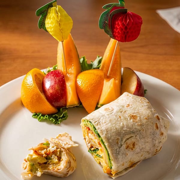 A white plate with a sliced wrap and a fruit salad featuring melon, oranges, and apples.