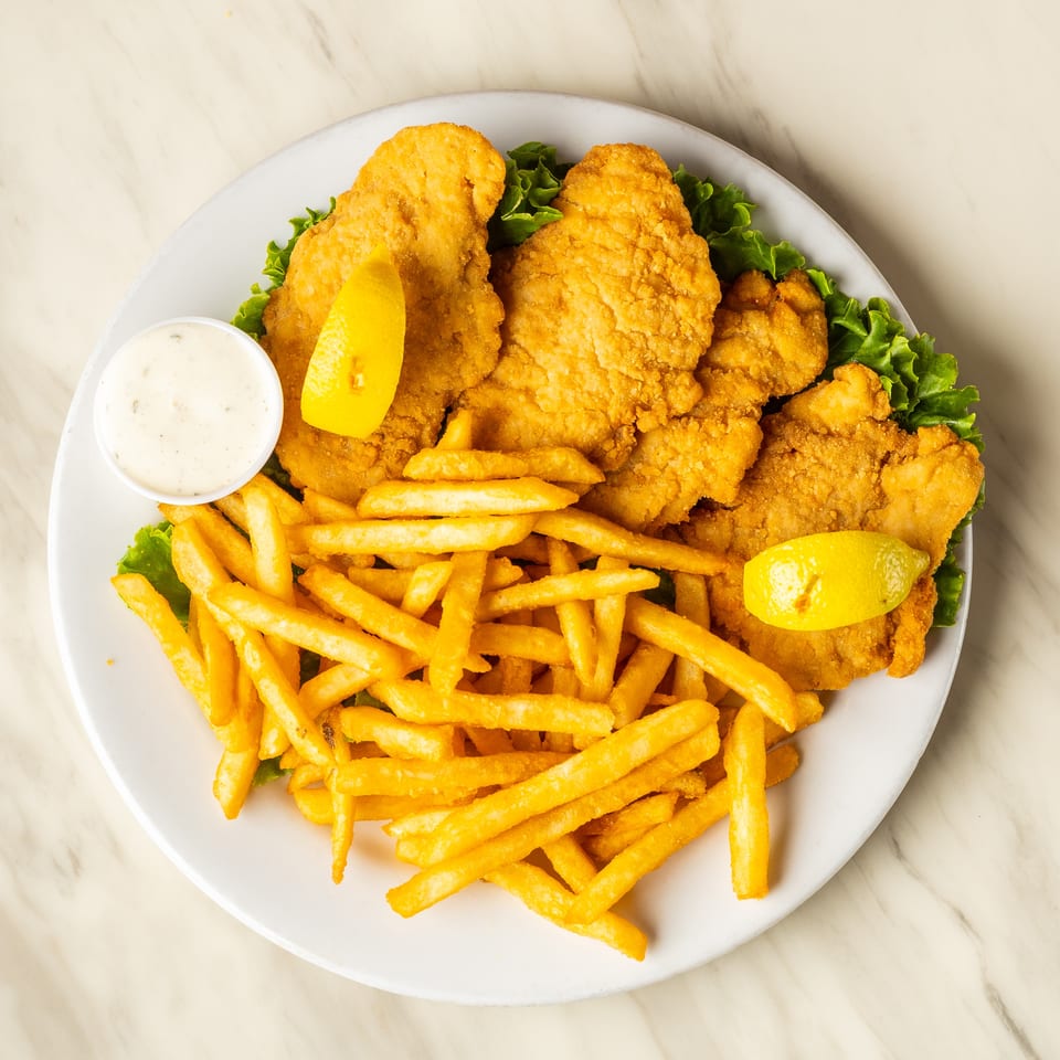 Golden fried fish fillets and french fries with lemon wedges and tartar sauce on a white plate.