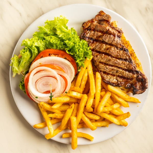Grilled steak with french fries, lettuce, tomato, and onion on a white plate.